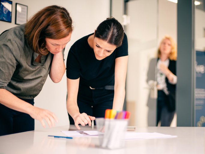 Two women leaning over table, discussing notes during client requirement workshop