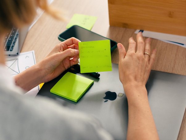 Hand holding post-it note over laptop