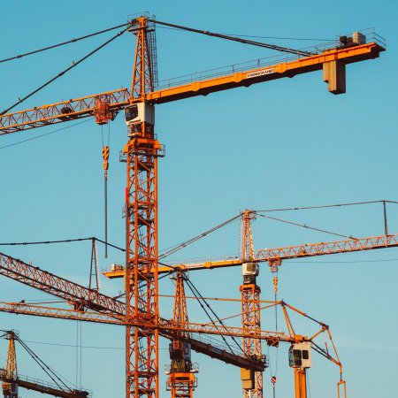 Multiple orange construction building cranes against blue sky